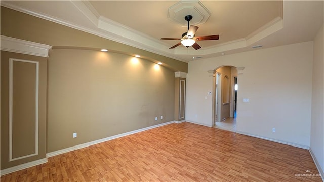 empty room with arched walkways, ceiling fan, light wood-style floors, a tray ceiling, and crown molding