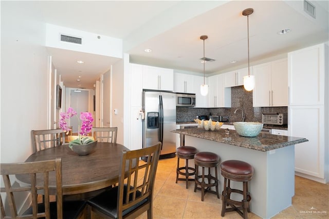 kitchen with pendant lighting, white cabinets, decorative backsplash, dark stone countertops, and stainless steel appliances