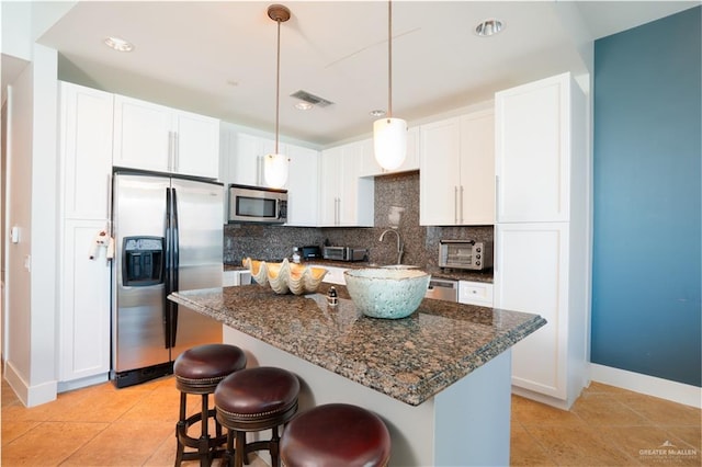 kitchen featuring dark stone counters, white cabinets, appliances with stainless steel finishes, tasteful backsplash, and light tile patterned flooring