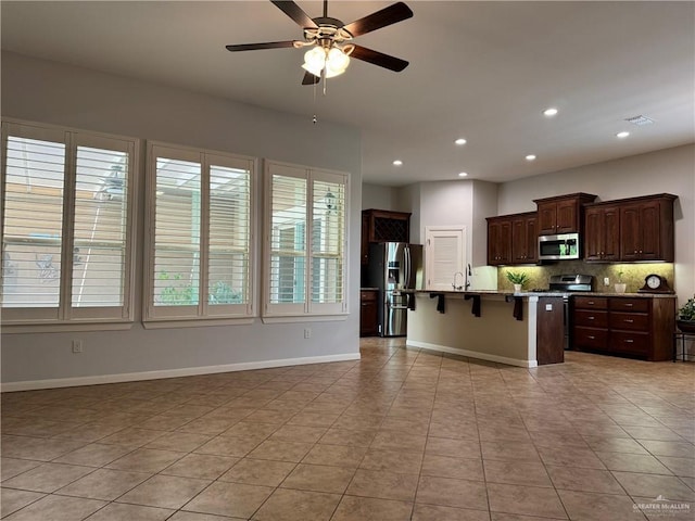 kitchen featuring a kitchen breakfast bar, tasteful backsplash, a center island with sink, light tile patterned floors, and appliances with stainless steel finishes