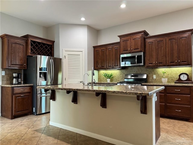 kitchen with a breakfast bar, decorative backsplash, an island with sink, appliances with stainless steel finishes, and light stone counters