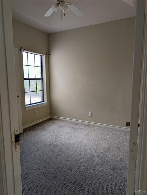 carpeted spare room with a ceiling fan and baseboards