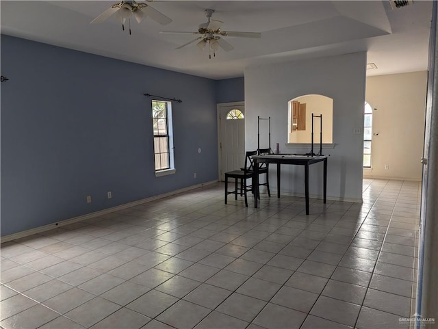 dining space featuring ceiling fan, arched walkways, tile patterned flooring, and baseboards