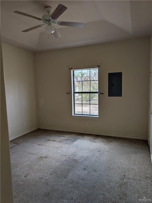 carpeted empty room with a ceiling fan, a raised ceiling, electric panel, and baseboards