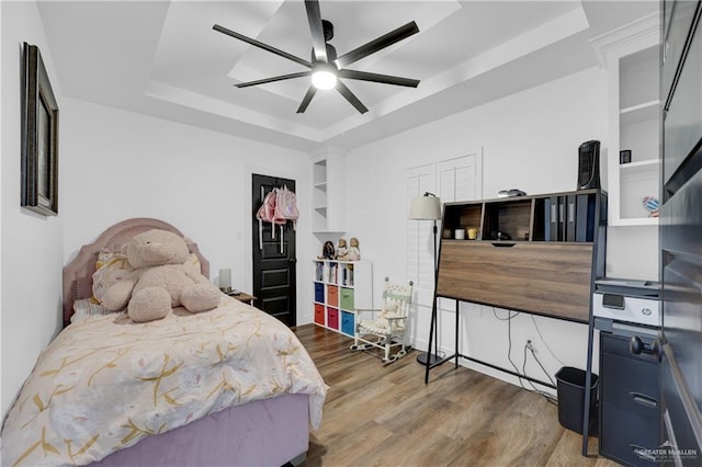 bedroom with dark hardwood / wood-style flooring, ceiling fan, and a tray ceiling