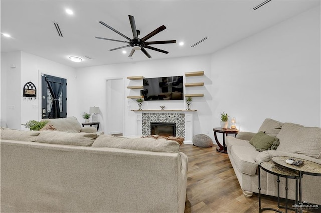 living room featuring a tiled fireplace, ceiling fan, and light hardwood / wood-style flooring