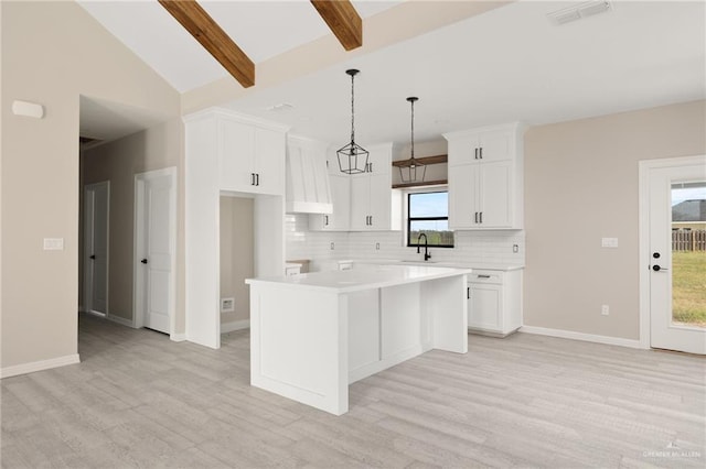 kitchen featuring a kitchen island, beamed ceiling, light hardwood / wood-style floors, decorative light fixtures, and white cabinets