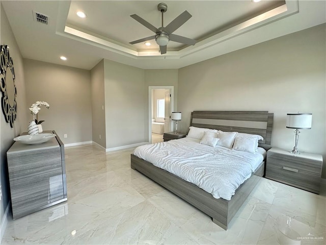 bedroom featuring a tray ceiling, ensuite bath, and ceiling fan