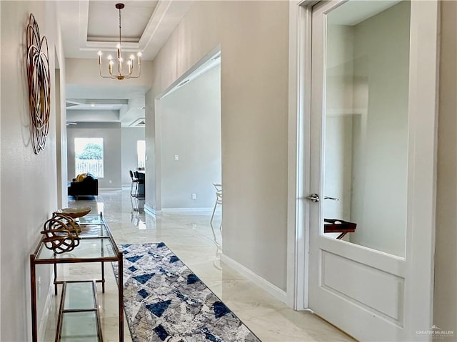 hallway featuring a tray ceiling and a chandelier