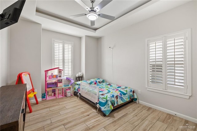 bedroom with ceiling fan, light hardwood / wood-style floors, and a tray ceiling