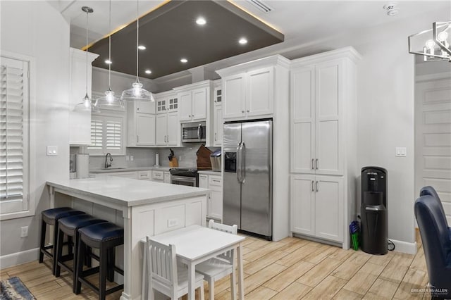 kitchen featuring pendant lighting, sink, kitchen peninsula, appliances with stainless steel finishes, and white cabinetry