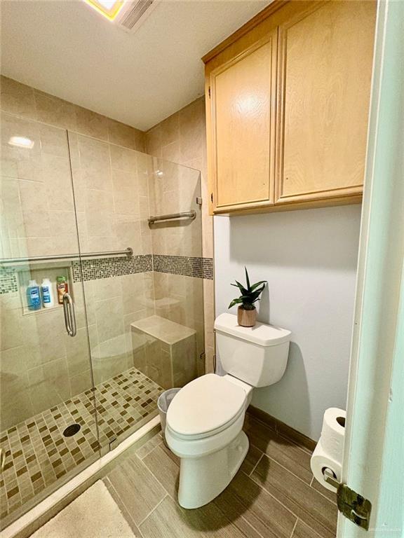 bathroom with a shower stall, baseboards, wood tiled floor, and toilet