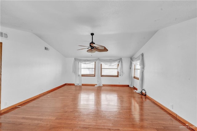 empty room with light wood-type flooring, a ceiling fan, a wealth of natural light, and lofted ceiling