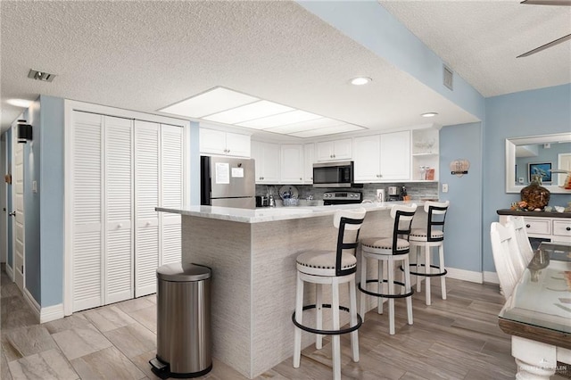 3000 Gulf Blvd Unit 701, South Padre Island, TX 78597 - kitchen featuring stainless steel appliances, open shelves, a textured ceiling, a peninsula, and white cabinets