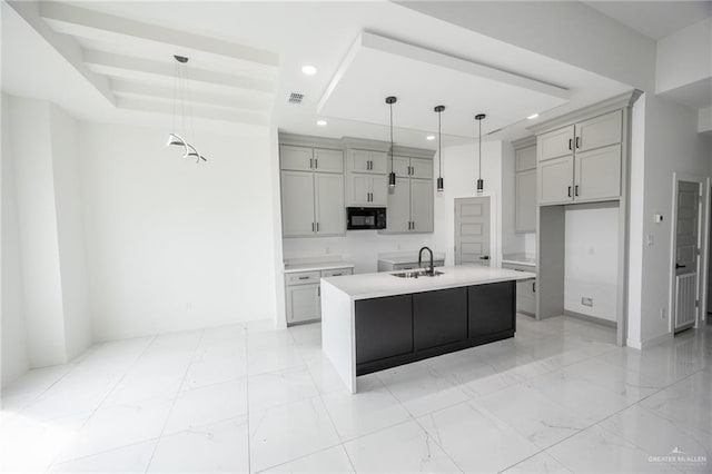 kitchen with decorative light fixtures, a kitchen island with sink, a tray ceiling, and gray cabinetry