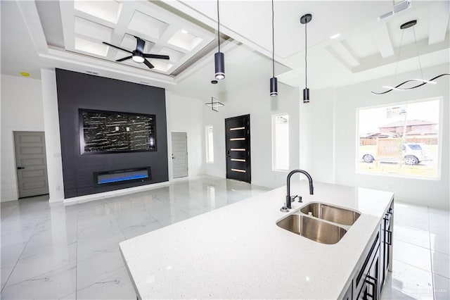 kitchen with light stone countertops, sink, hanging light fixtures, and a kitchen island with sink