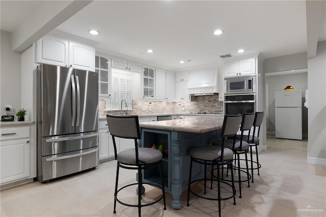 kitchen with decorative backsplash, custom exhaust hood, stainless steel appliances, white cabinets, and a kitchen island