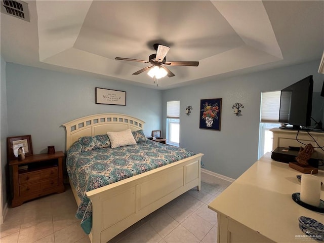 bedroom with ceiling fan, a tray ceiling, and light tile patterned floors