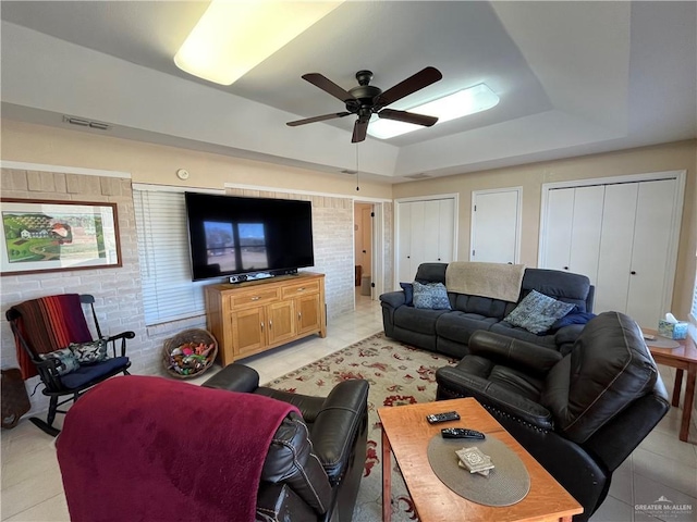 living room featuring light tile patterned flooring, ceiling fan, and a tray ceiling