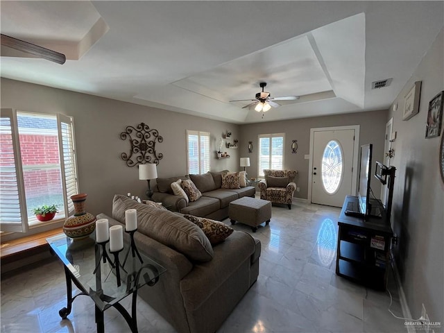 living room with a raised ceiling, a wealth of natural light, and ceiling fan