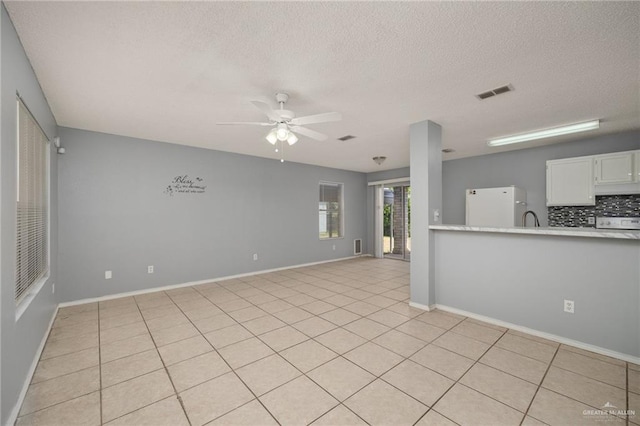 unfurnished living room featuring ceiling fan, light tile patterned flooring, sink, and a textured ceiling