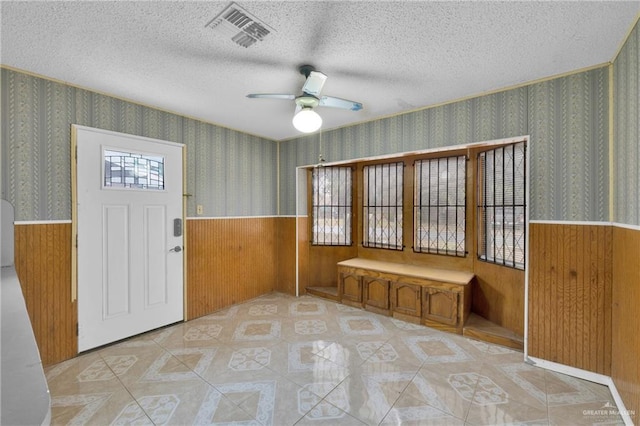 foyer entrance featuring a wainscoted wall, visible vents, a textured ceiling, and wallpapered walls