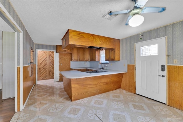 kitchen with a peninsula, wallpapered walls, light countertops, and wainscoting