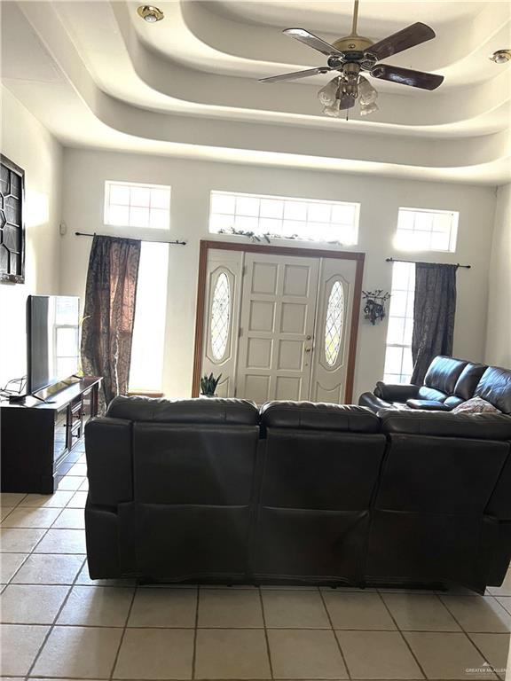 tiled living room featuring ceiling fan, a healthy amount of sunlight, and a tray ceiling