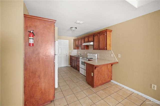 kitchen with white appliances, tasteful backsplash, a peninsula, light countertops, and under cabinet range hood