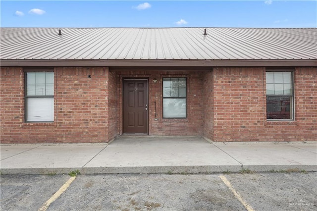 property entrance with uncovered parking, brick siding, and metal roof