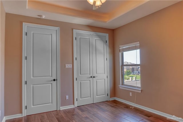 unfurnished bedroom featuring ceiling fan, a raised ceiling, and light wood-type flooring