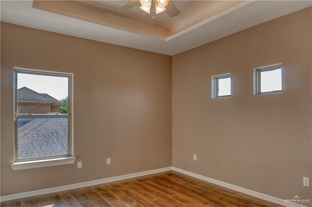 spare room with ceiling fan, a raised ceiling, and wood-type flooring