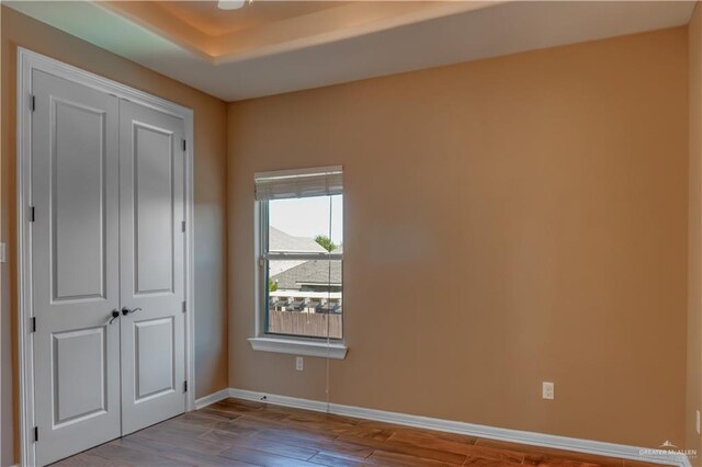 unfurnished bedroom with a raised ceiling, light hardwood / wood-style flooring, and a closet