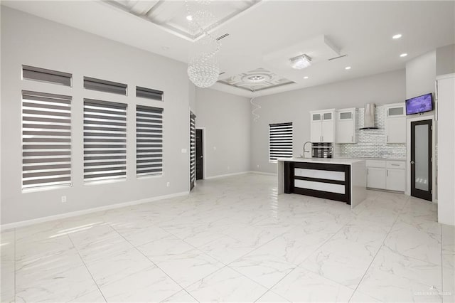 kitchen with tasteful backsplash, white cabinetry, an island with sink, sink, and wall chimney exhaust hood