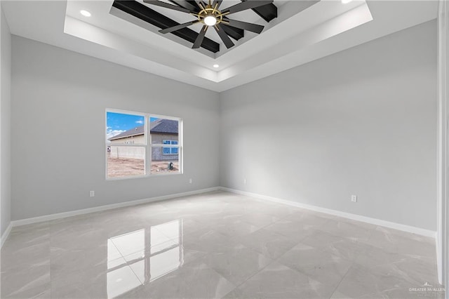 empty room with ceiling fan and a tray ceiling