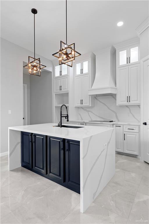 kitchen featuring wall chimney exhaust hood, decorative light fixtures, a center island with sink, and white cabinets