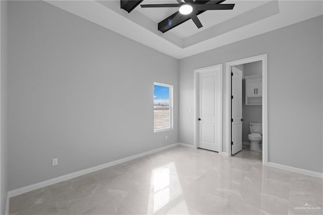 unfurnished bedroom with ensuite bathroom, ceiling fan, and a tray ceiling