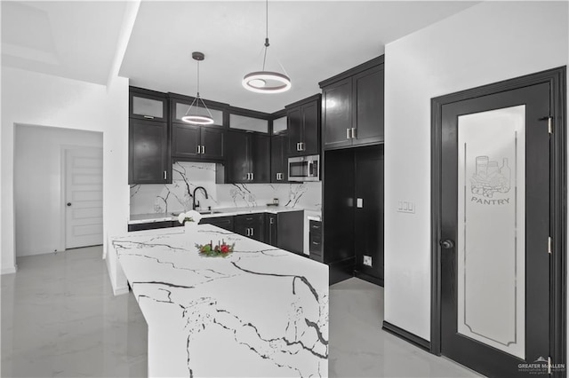 kitchen with marble finish floor, stainless steel microwave, decorative backsplash, light stone countertops, and dark cabinets