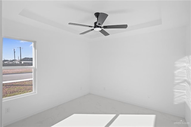 empty room featuring a ceiling fan, a raised ceiling, and a healthy amount of sunlight