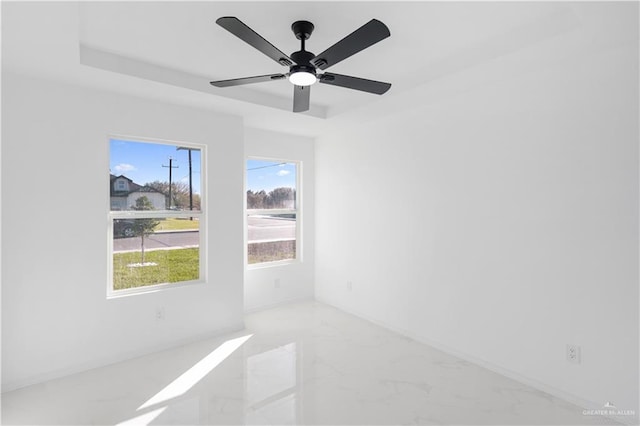 unfurnished room with a raised ceiling, ceiling fan, and marble finish floor