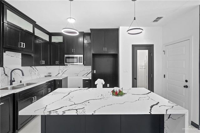 kitchen featuring light stone countertops, dark cabinets, stainless steel microwave, and a sink