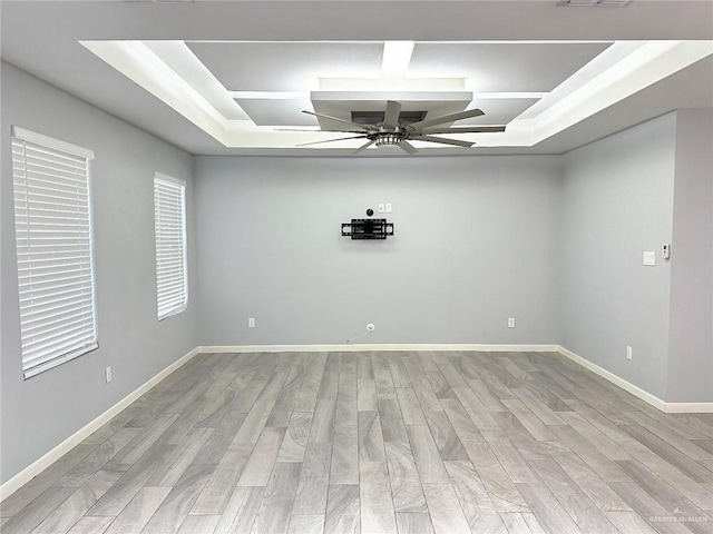 spare room featuring a tray ceiling, wood finished floors, a ceiling fan, and baseboards