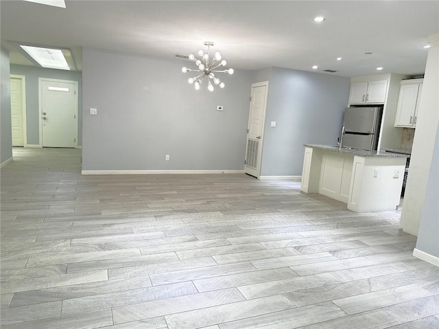 interior space featuring white cabinets, freestanding refrigerator, light stone countertops, an inviting chandelier, and light wood-style floors