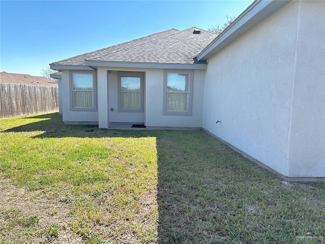 back of property with stucco siding, a shingled roof, fence, and a yard