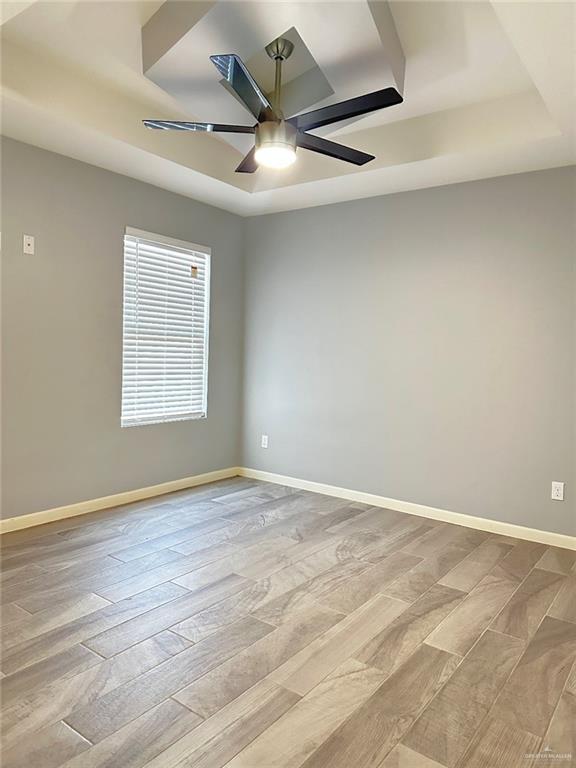 spare room featuring ceiling fan, baseboards, a raised ceiling, and light wood-style floors