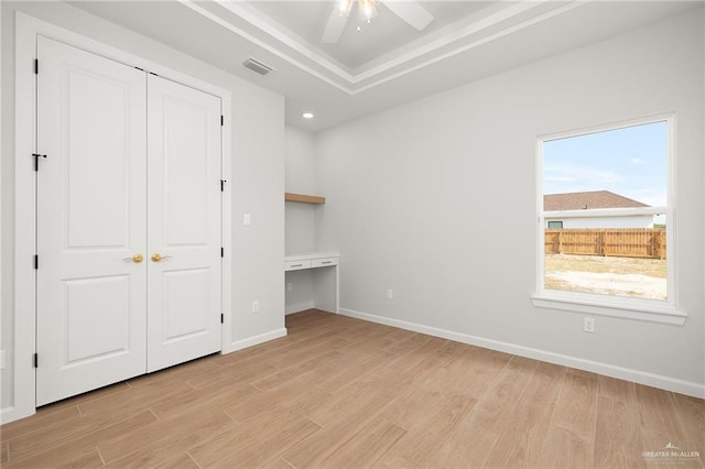 unfurnished bedroom with a closet, ceiling fan, light wood-type flooring, and a tray ceiling