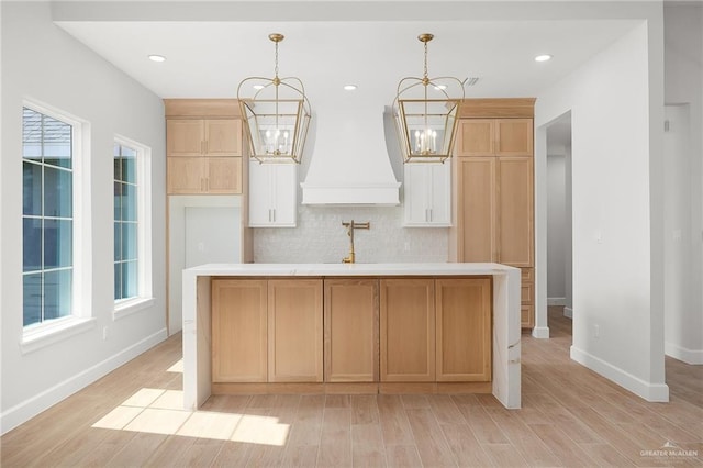 kitchen featuring an inviting chandelier, pendant lighting, custom range hood, and an island with sink