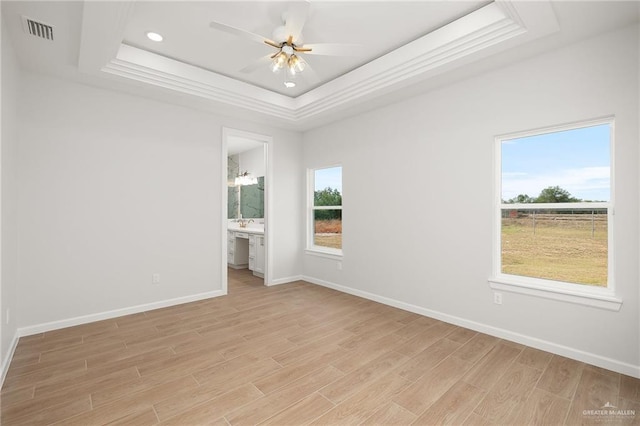 empty room with a raised ceiling, ceiling fan, and light wood-type flooring