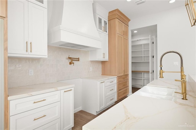 kitchen featuring premium range hood, white cabinetry, tasteful backsplash, light stone countertops, and hardwood / wood-style floors