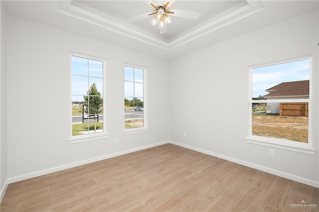 empty room featuring ceiling fan, a tray ceiling, and light hardwood / wood-style floors